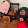 Collection of hats and a wallet with 'KC Laser Co' branding on a wooden surface.