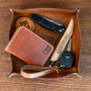 Leather tray with wallet, knife, and other items on a wooden surface