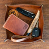Leather tray with wallet, knife, and other items on a wooden surface
