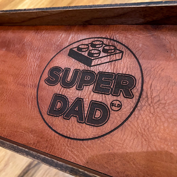 Brown leather tray with 'Super Dad' engraving on a wooden surface